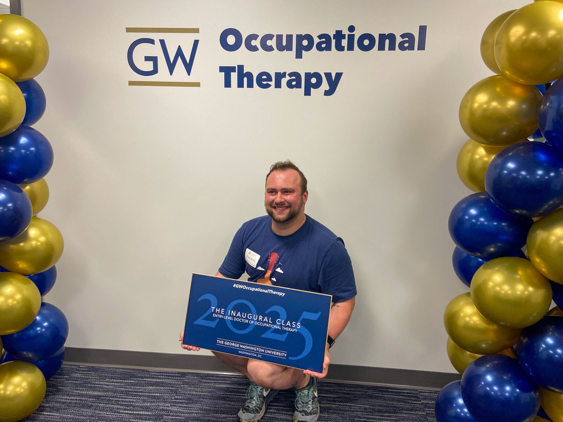 Student holding Inaugural Class sign in front of GW OT Logo