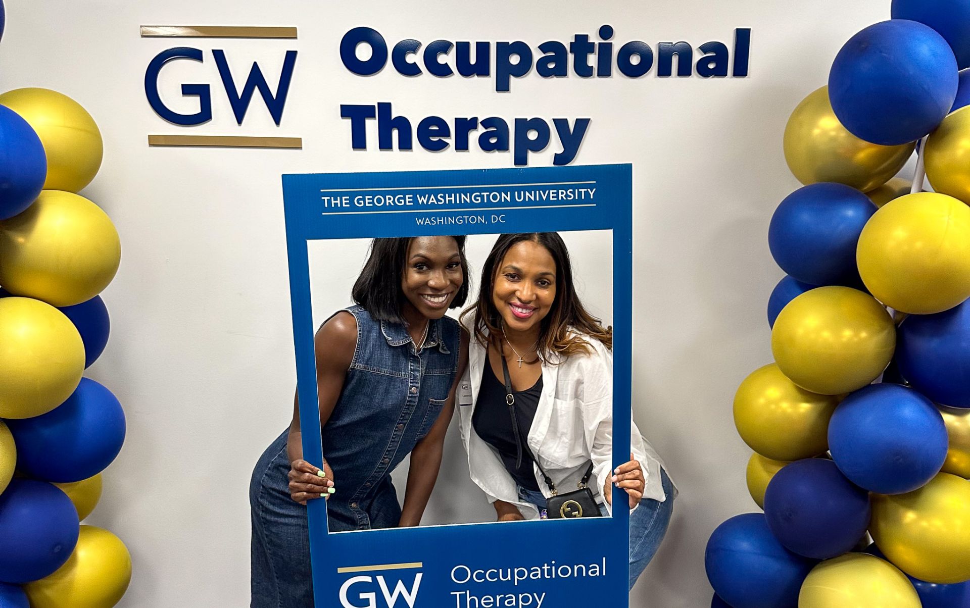 student and friend holding GW OT letters smiling in front of sign