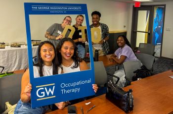 7 GW OT Students in Blue Picture Frame Prop holding OTD gold letters_437x287